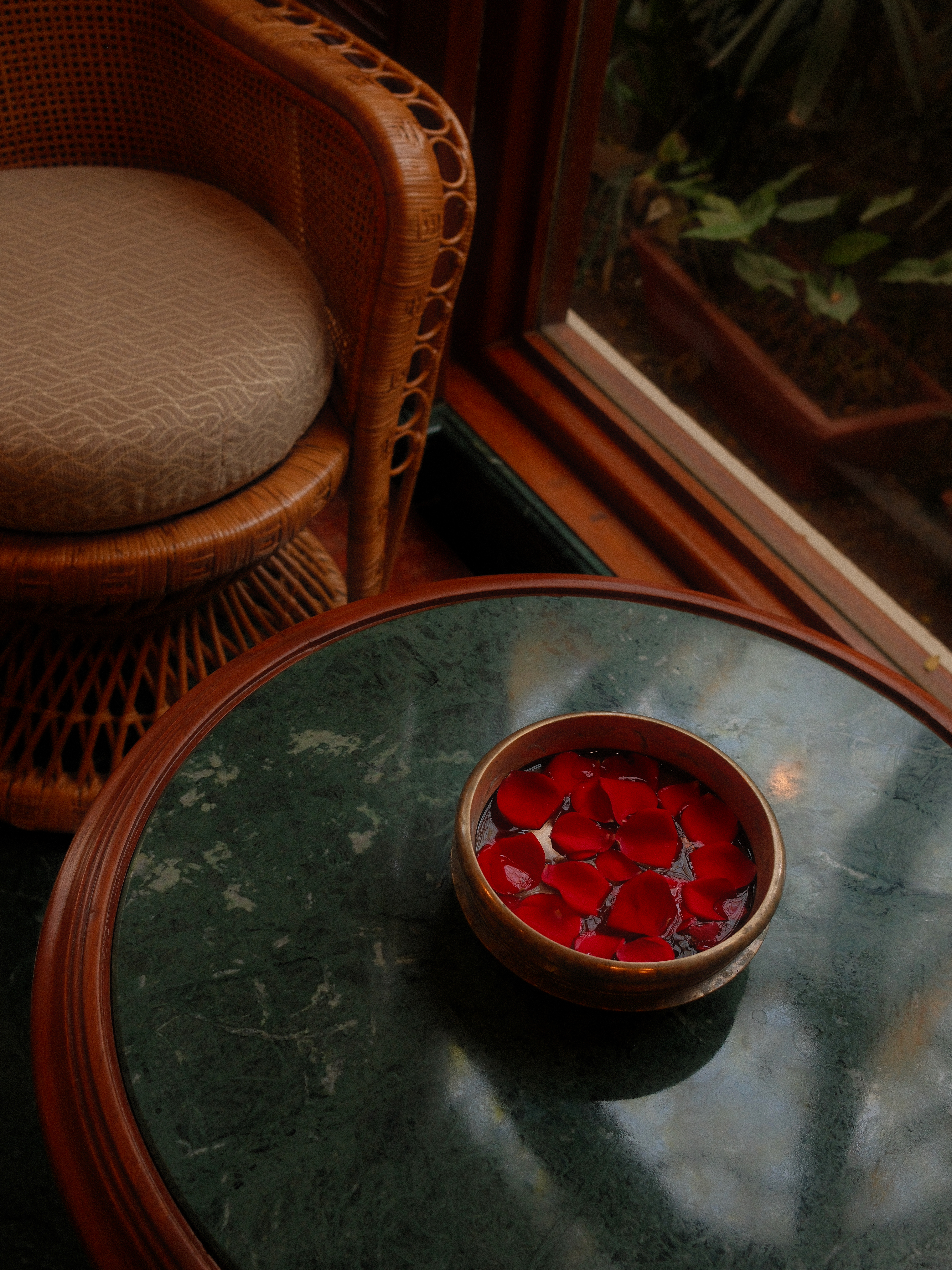 Brass bowl with deep red rose petals on green marble table, warm natural light